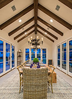 Modern dining room with high, vaulted ceilings with exposed beams, custom chandalier, surrounding windows with french doors, and 14-person table