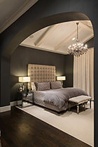 Master bedroom with vaulted ceiling, painted beams, arched entry, and hardwood floors